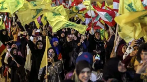 EPA Hezbollah supporters wave Hezbollah flags as they listen to the speech of Hezbollah leader Hassan Nasrallah via a giant screen in southern suburb of Beirut, Lebanon, 14 August 2018