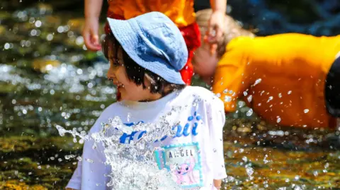 Grasmere Primary School A girl wearing a denim bucket hat and a white t-shirt looks to one side smiling, as water is splashed in front of her.
