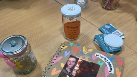 Decorated glass jars with lids are on a wooden table as well as photo memory book with pictures of a girl on it
