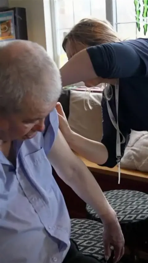 A man in a light, button-up shirt getting a jab from a person in a navy shirt.