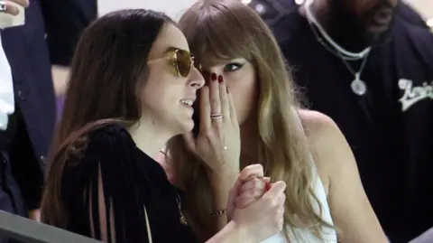 Penyanyi Reuters Taylor Swift berbicara dengan musisi dan aktris, Alana Haim di tribun