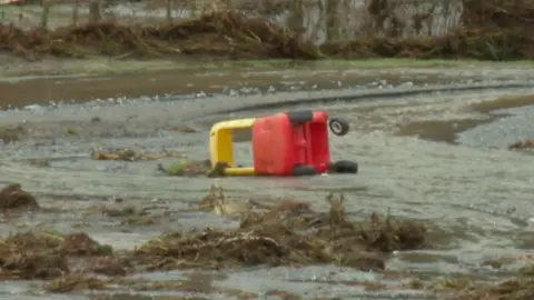 A red and yellow child's car on it's side surrounded by water