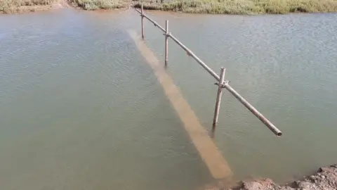 A WOODEN BRIDGE SEEN PARTIALLY COVERED IN WATER AT HIGH TIDE