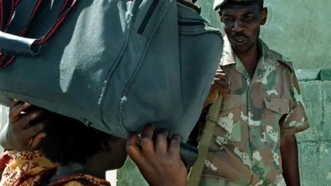 AFP A South African soldier checks the passports of Zimbabwean citizens who walk across the Beit Bridge border post between the two countries to buy food 07 January 2003. More and more Zimbabweans are venturing across the border to buy basic foods such as fruits and Maize meal, which is not available in Zimbabwe.