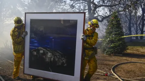 EPA Firefighters remove a painting as they continue to extinguish fires in a home during the "Skirball Fire"