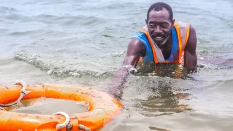 BBC Lifeguard Nicholas Paul swimming with a lifebuoy in Lagos, Nigeria