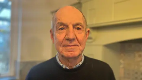 John Coyne, wearing a sweater and shirt standing in his renovated home