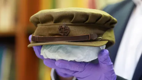 PA Media A curator holds an Auxiliary Territorial Service hat worn by Dame Vera Lynn. The curator is wearing gloves and the hat is supported by padding underneath in the close-up photograph.