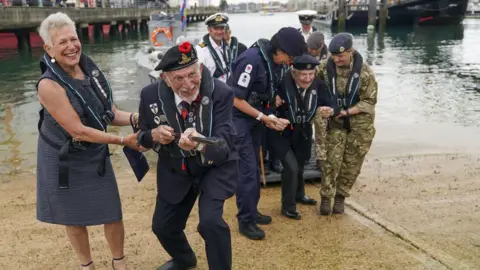 Steve Parsons Joe Cattini raising his walking stick like a machine gun as he and other veterans are welcomed to the Portsmouth Historic Dockyard to commemorate the 77th anniversary of the Normandy Landings in 2021