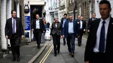 Getty Images Britain's Prime Minister Theresa May (C) is flanked by security guards as she walks in Mevagissey, south-west England, during the 2017 election campaign