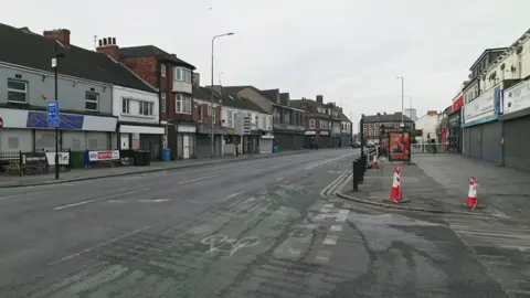 A view of the scene, with traffic cones on the side of the road by a junction.