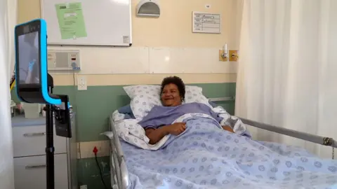 A patient laying in bed using a robot monitor