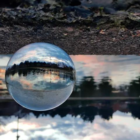 Charlotte Harneiss A sphere shaped clear ball showing sunset landscape against an up-side down background