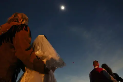 Mario Tama/Getty Images Couples view the solar eclipse during totality at a mass wedding at the Total Eclipse of the Heart festival on April 8, 2024 in Russellville, Arkansas.