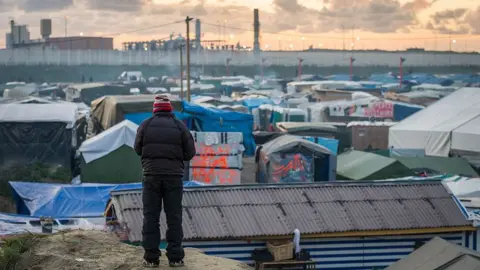 Getty Images A refugee stands on a hill overlooking the Calais 'junge' camp in Calais