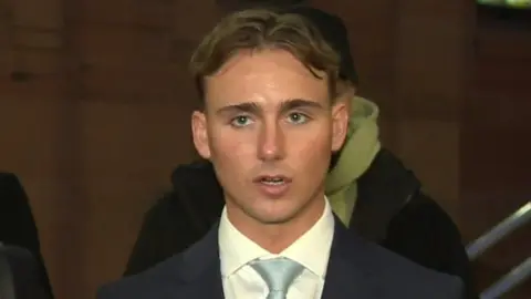 A young man in a suit speaks outside a court