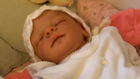 A lifelike reborn doll in a cot