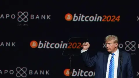 Reuters Donald Trump in a navy blue suit and royal blue striped tie holding his fist up during a Bitcoin-sponsored event at which he spoke. 