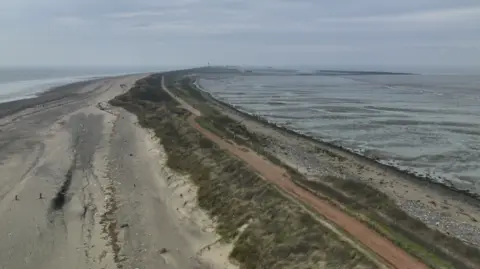 A road, crumbled by the sea, along a peninsula. Either side is sand and sea. 