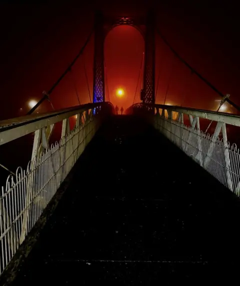 David Lee Two people are silhouetted against a red sky on the suspension bridge in Inverness.