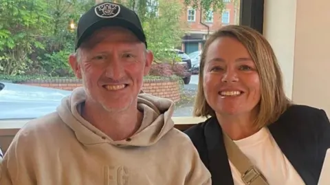 John and Lorna are sitting in front of a window and are smiling at the camera. 
