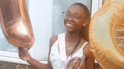 Hannah Jacobs wearing a white patterned dress and glasses and holding balloons