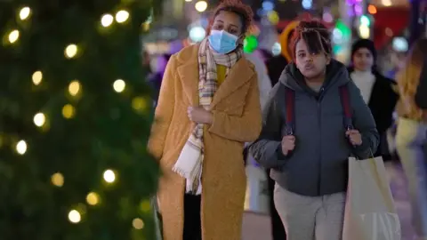 PA Media Two women, one wearing a mask, walk on Oxford Street, London