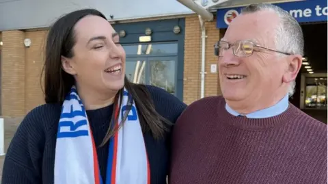 EFL/BHF A picture of Pippa Sharman, wearing a white, red and blue Reading scarf and a blue jumper, stood next to David Norman, who is wearing a maroon jumper and blue shirt.