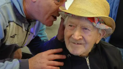 Ron "Ginger" Parsons smiles as a man whispers in his ear