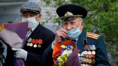 Reuters Belarusian veterans Pyotr Vorobyov and Pavel Eroshenko cover their faces with protective masks as they listen to a military band