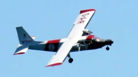 Channel Islands Air Search A red and white plane used by the Channel Islands Air Search team flying on a sunny and cloud free day over the Channel Islands.