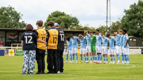 Cameron Murray Family members and footballers stand on the pitch with their heads bowed