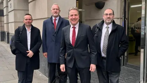 Weca Standing outside the Department for Transport in London are North Somerset Council leader Mike Bell, South Gloucestershire Council leader Ian Boulton, Metro Mayor Dan Norris, and Bristol City Council leader Tony Dyer. All four men are smiling at the camera and wearing dark suits