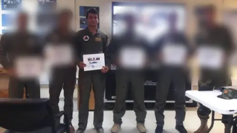 Mohammad Edris Momand Momand standing with colleagues holding a certificate displaying a helicopter
