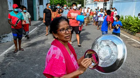 Getty Images A woman in a protest against food price hikes bangs dishes together.