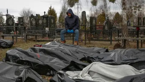 Reuters A funeral service employee sits next to bodies of civilians in Bucha