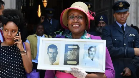 EPA Andria Marsh, 63, holds up photographs of her parents and her original British passport, following a Windrush service at Westminster Abbey