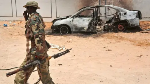 AFP A Somali soldier patrols next to the burnt-out wreckage of a car that was used by suspected al-shabab fighters on April 16, 2017.