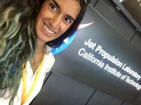 Farah Alibay/JPL/NASA A woman with dark brown and green hair stands in front of a sign reading 'Jet Propulsion Laboratory, California Institute of Technology