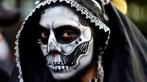 AFP A woman wears a black hood and make-up during the Catrinas parade in Mexico City.