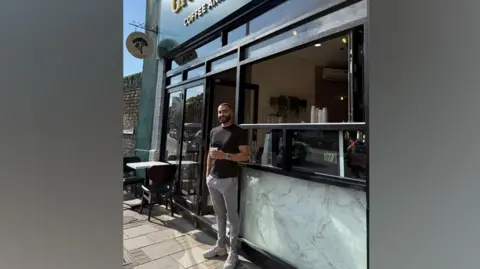 BBC/Rusty Nart Rusty Nart leans against the entrance to his coffee shop, holding a coffee 