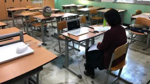 BBC A teacher sits in an empty classroom