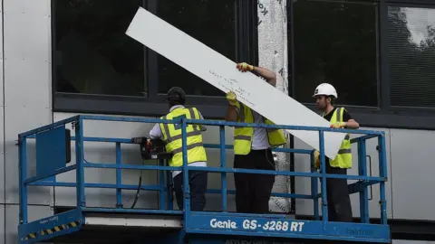 Getty Images Workers remove cladding for testing from one of the tower blocks in Salford