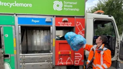 A recycling worker wearing orange hi-vis and putting recycling into a waste truck