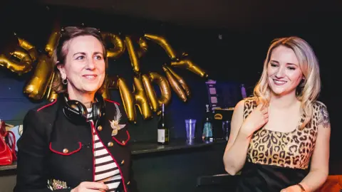 Pretty Ugly Kirsty Wark and Lynne Johnston behind the decks at a club night - Kirsty Wark is wearing a black jack with red trim and a black and white striped top. Lynne Johnston is wearing a leopard print-patterned dress