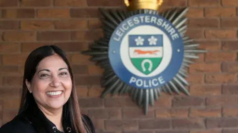 Supplied Rani Mahal is smiling at the camera. The Leicestershire Police badge is in the background against a brick wall.