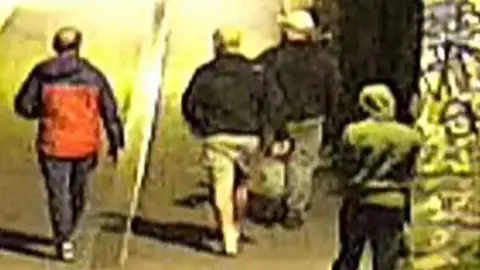 Avon and Somerset Police A CCTV image of four men in a street at night time. They are wearing dark clothing. Two are wearing caps, one has a green hoody on and one is bare headed and has a bald patch.
