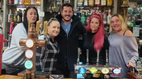 Dale Smith A group of people, made up of four women and one man, stand behind the bar at the Wheatsheaf Pub in Calne in Wiltshire