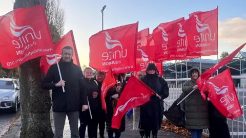 BBC Unite the Union members hold red flags on the picket line at Glenveagh school in south Belfast