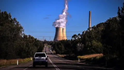 Getty Images A car drives towards smoke and steam rising from the Bayswater coal-powered thermal power station located near the central New South Wales town of Muswellbrook, New South Wales, Australia